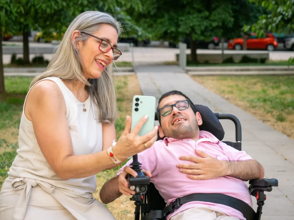 Disabled man in wheelchair looking at mobile phone with support worker